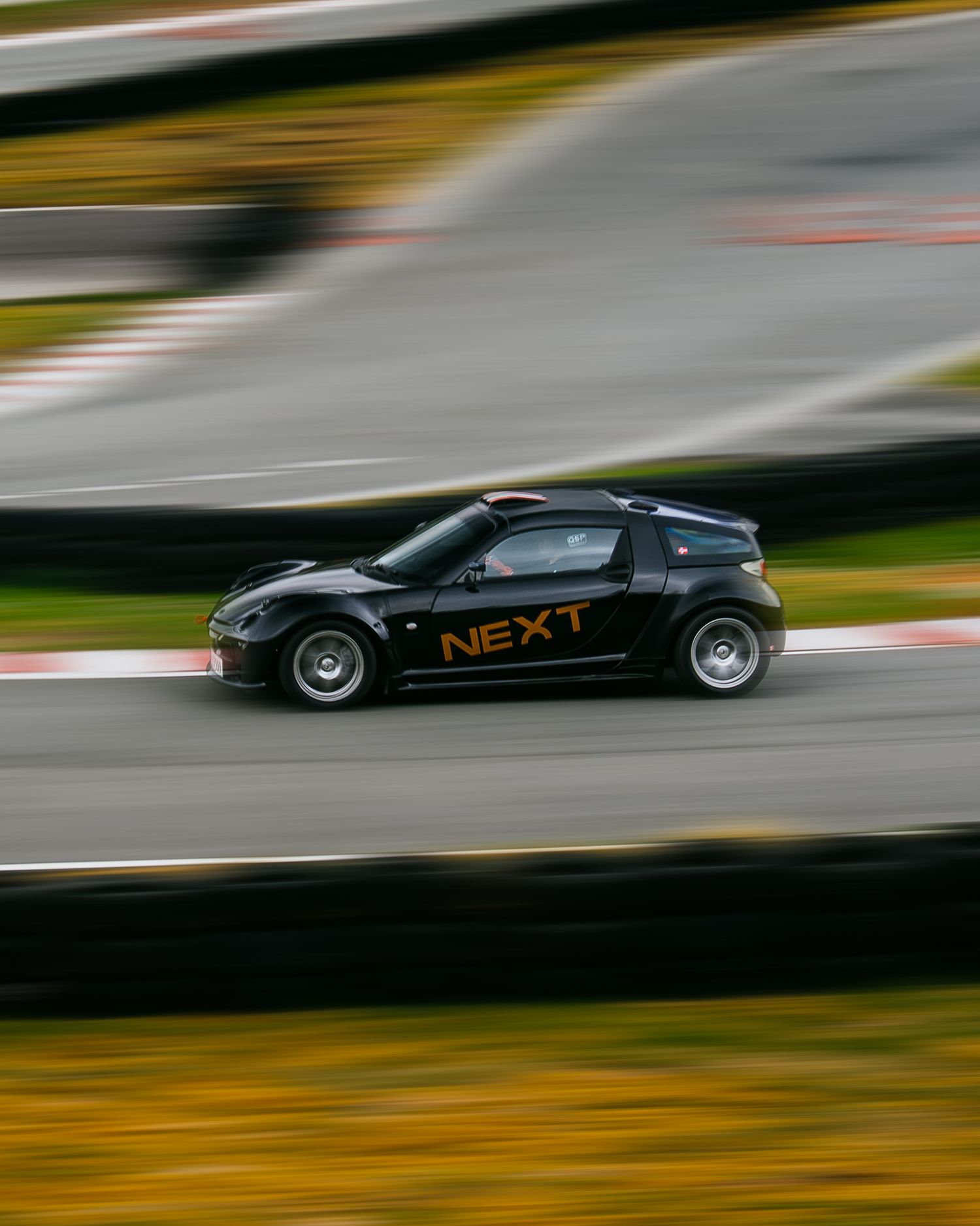 Black racing car speeds along a racetrack with motion blur effect creating a dramatic sense of movement and speed.