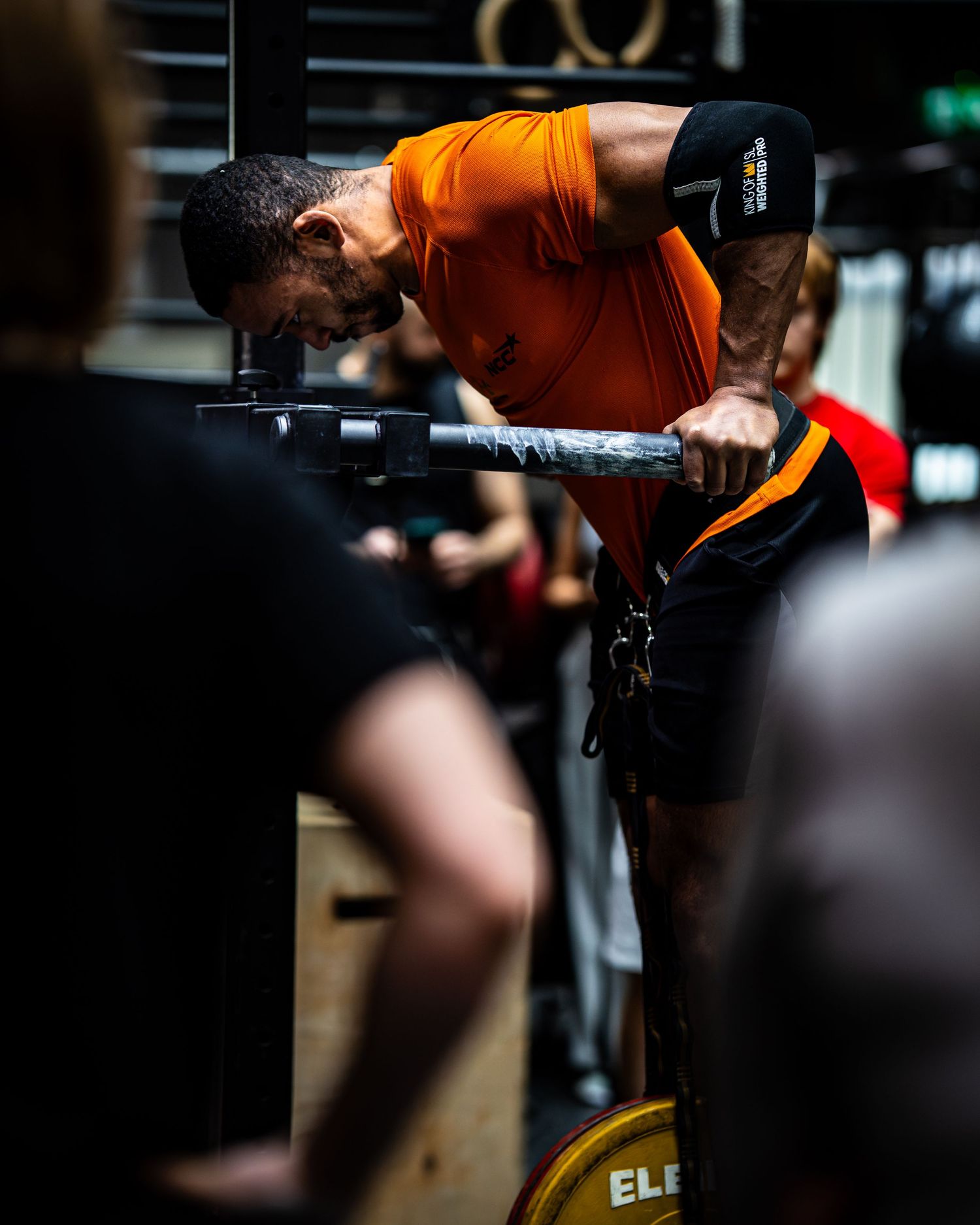 Person in orange shirt doing weighted dips exercise with Eleiko plates in dark gym setting.
