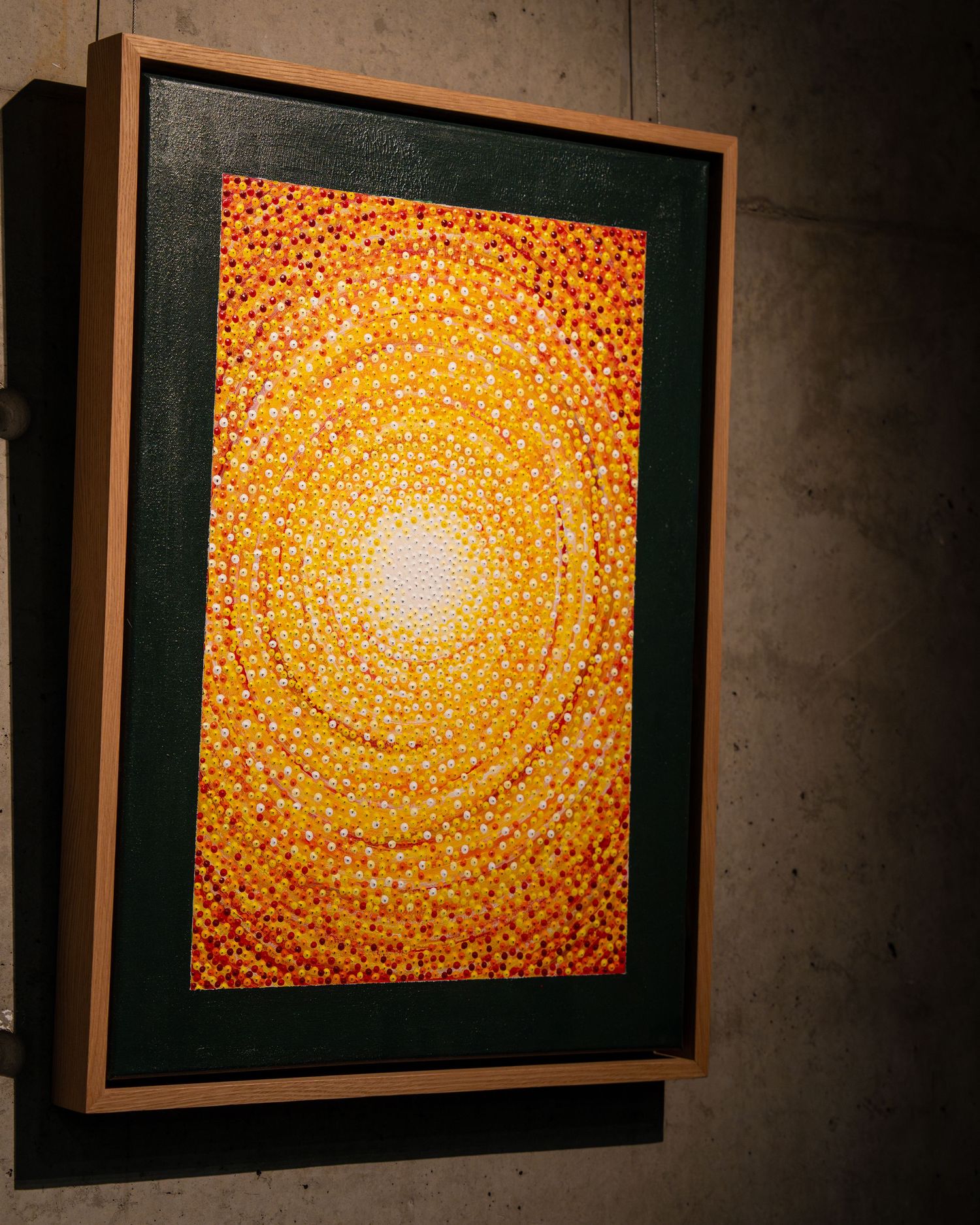 Framed artwork displaying a mesmerizing orange and yellow spiral pattern made of dots.