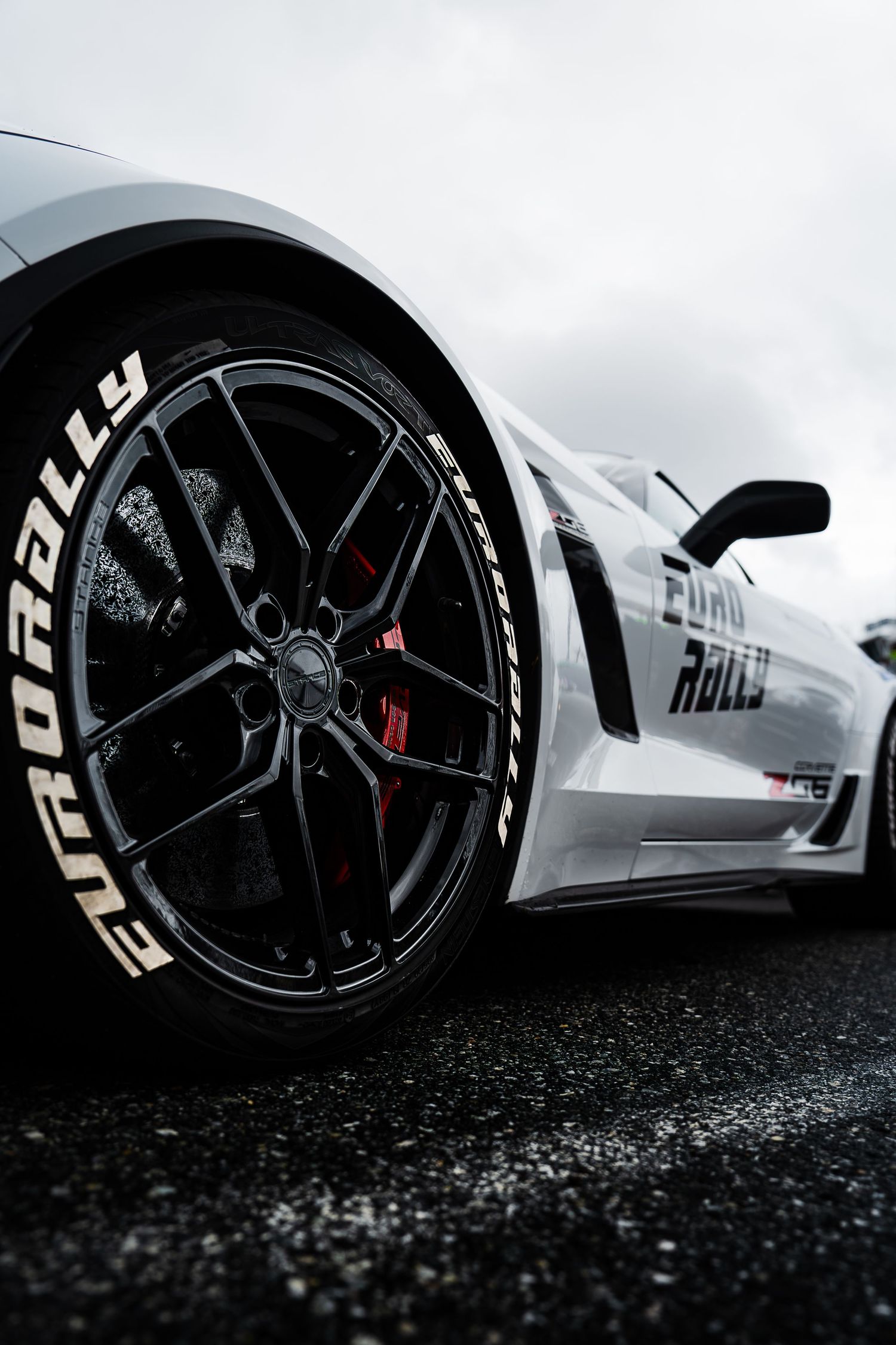 Close-up shot of a black sports car wheel with Toyo Rally tire branding on wet asphalt.