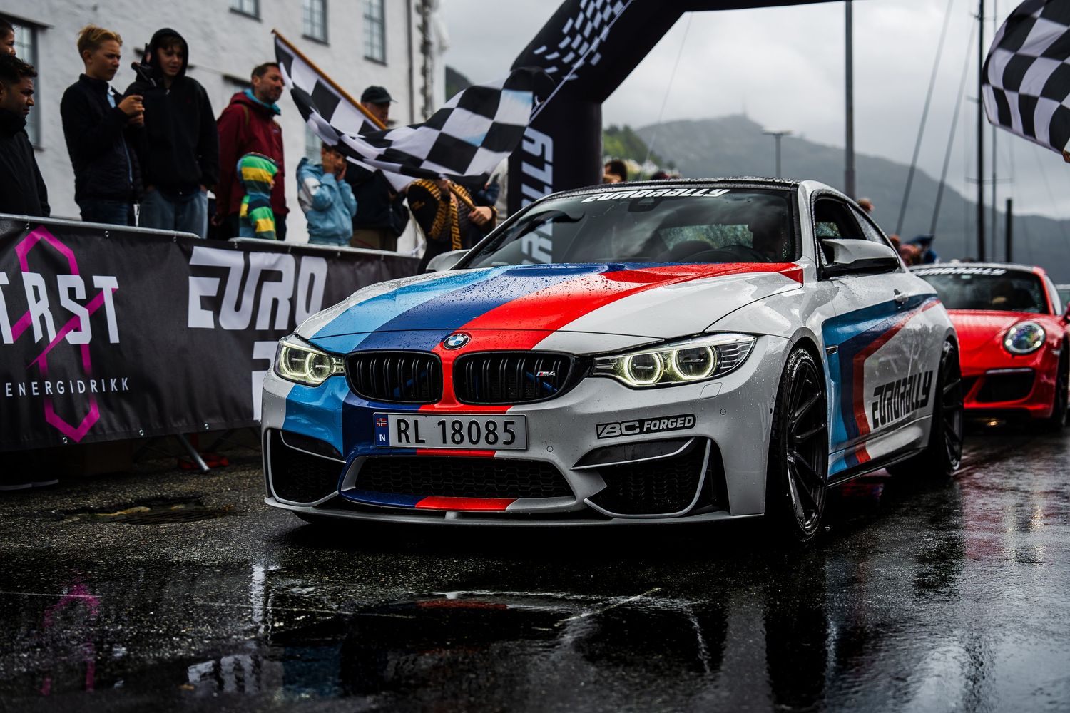 BMW M4 in motorsport livery featuring blue, red and white racing stripes under Eurorally arch.