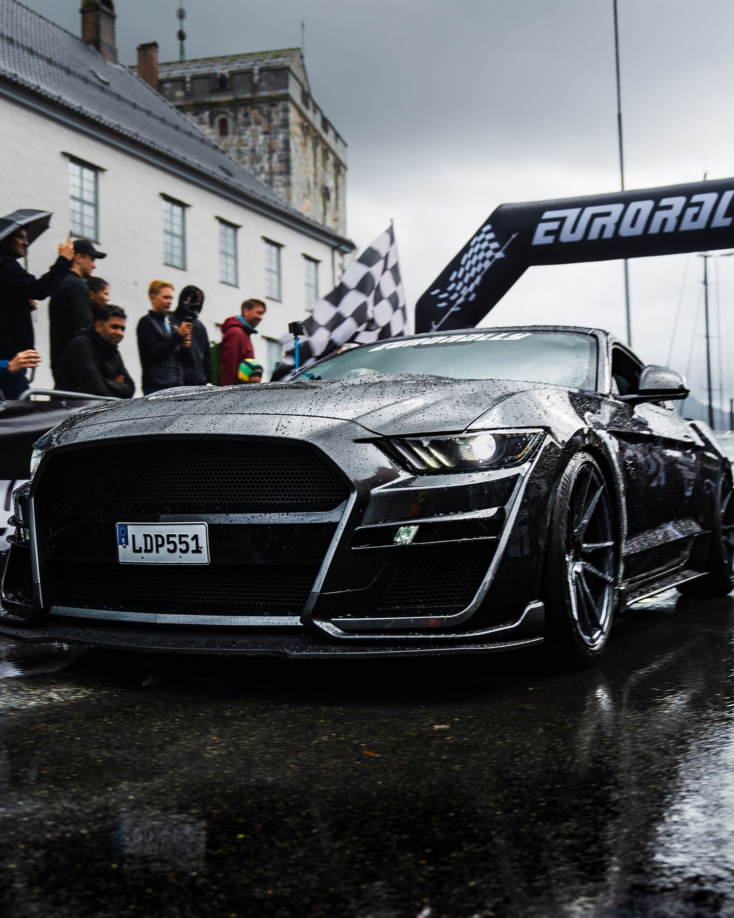 Black Ford Mustang Shelby GT500 crossing finish line at Eurorally event in the rain.