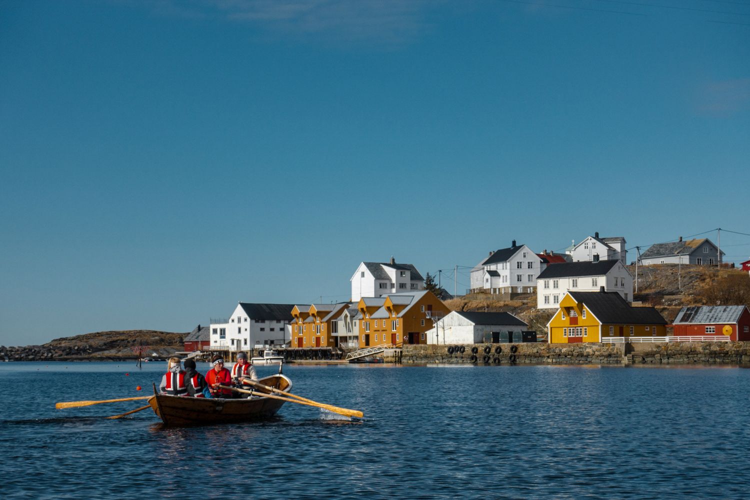 Colorful coastal houses line the waterfront as a red boat cruises past in a Norwegian fishing village.