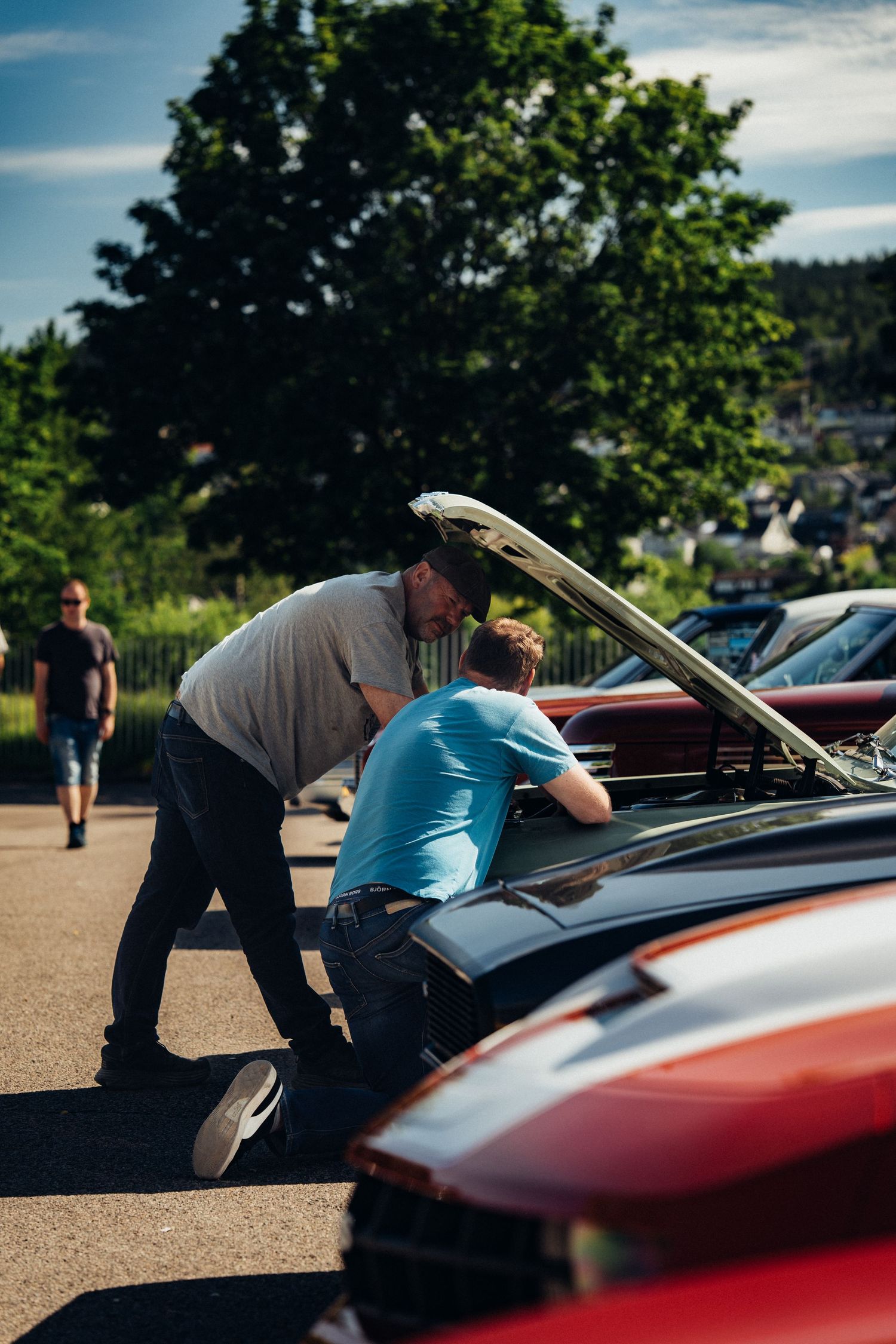 Car enthusiasts examining under the hood at classic car show on sunny day.