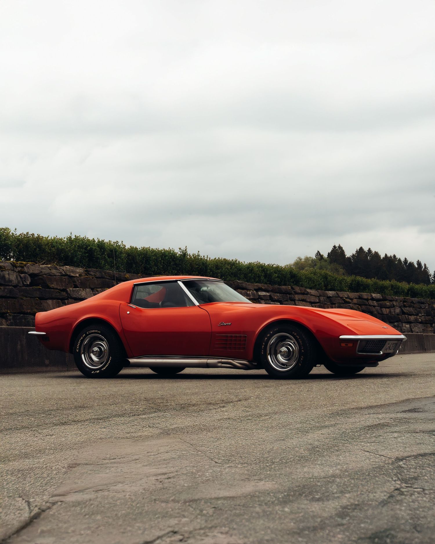 A red vintage Ferrari sports car parked on a concrete surface with trees in the background.