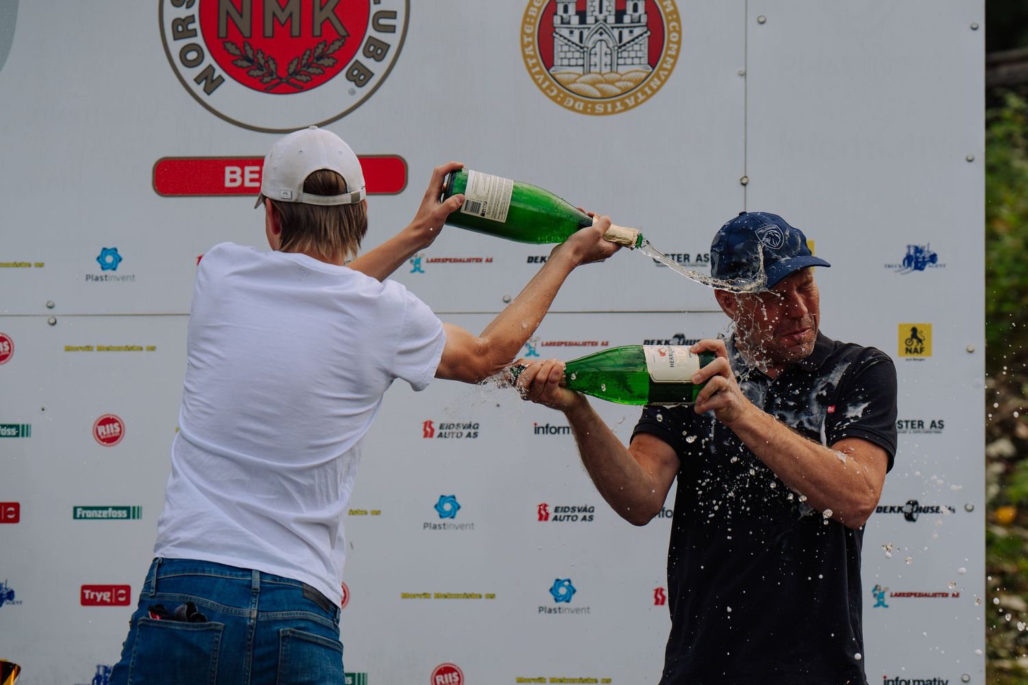 Two people compete in a water balloon toss competition at an outdoor event with sponsor banners in the background.