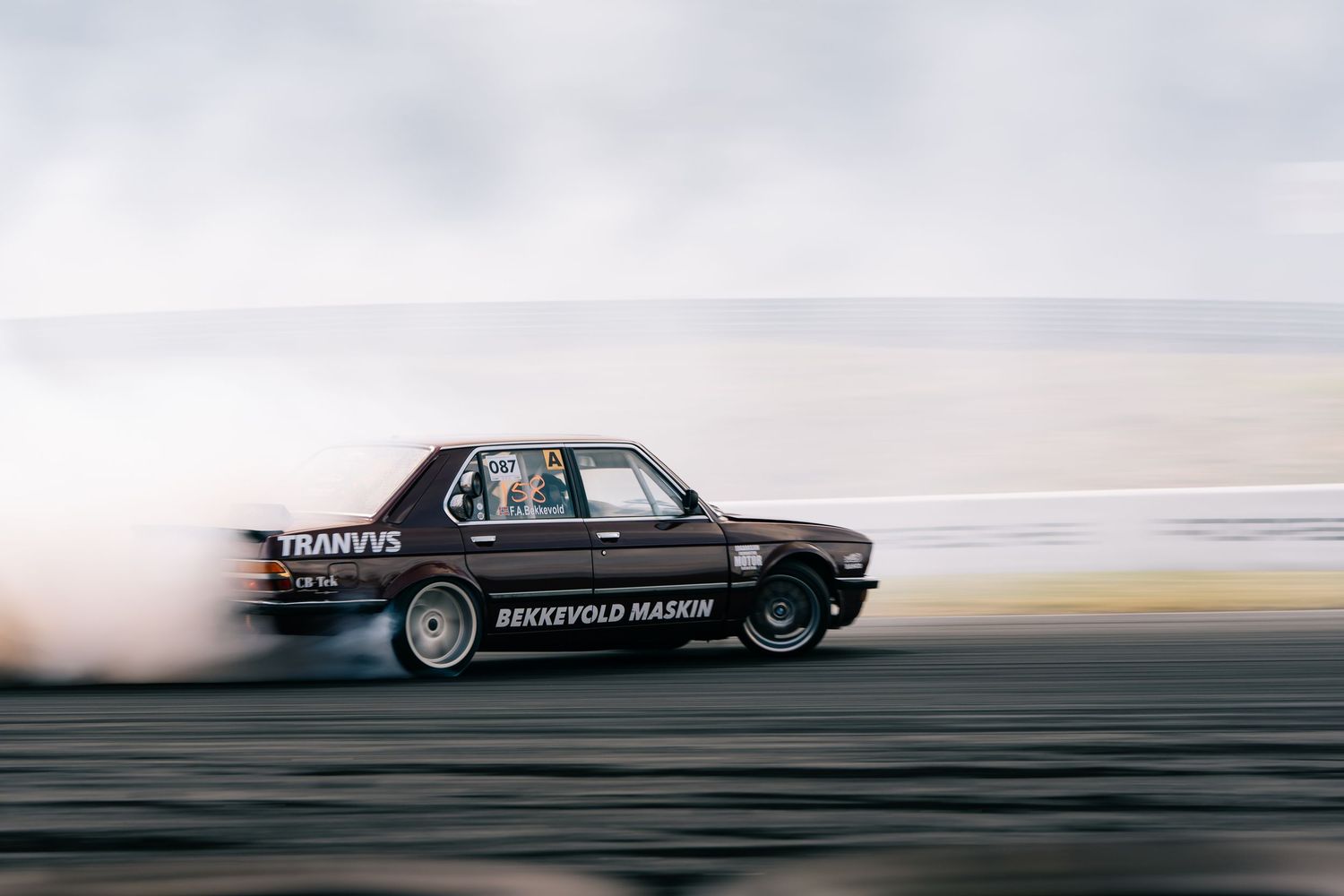 Black BMW drifting on a racetrack creating smoke clouds during a performance driving demonstration.