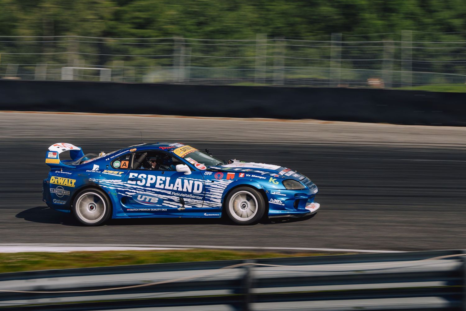Blue race car drifts around a track during a professional motorsport competition with smoke trailing behind.