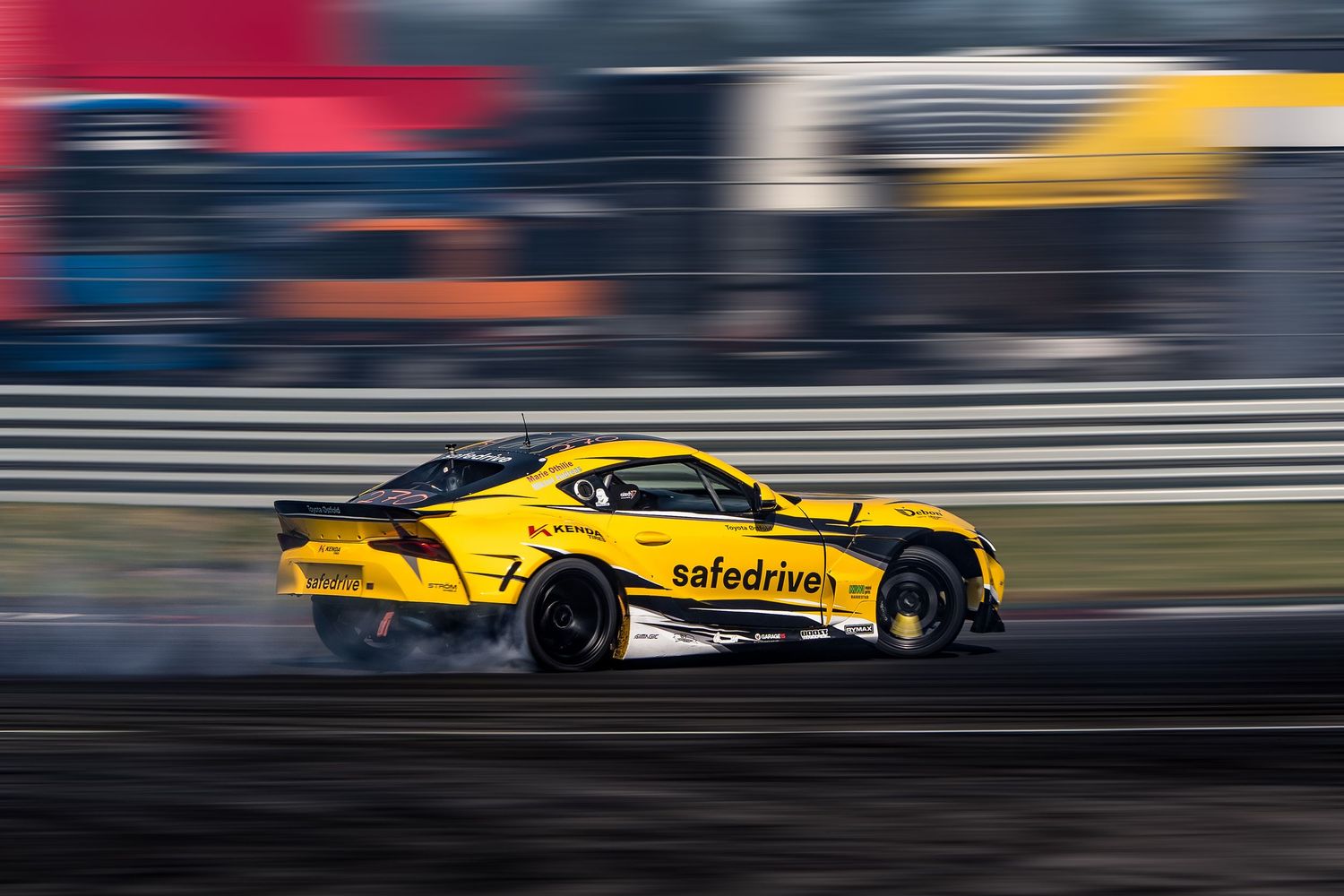 Yellow race car drifts around track corner with smoke trailing behind during competitive motorsport event.