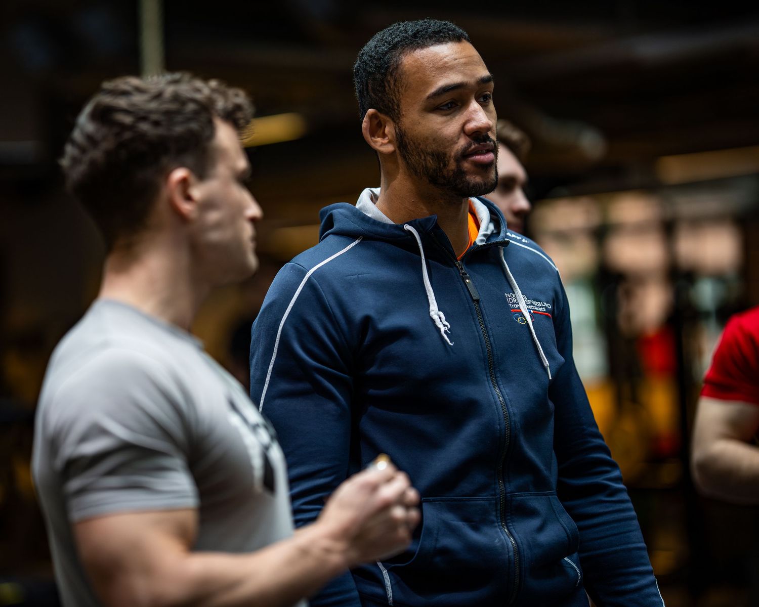 Athletes engaged in casual conversation during workout session in gym environment.