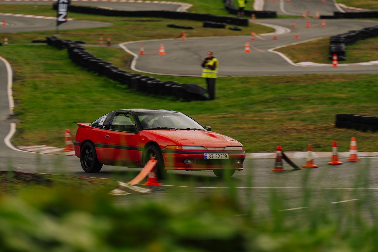 Red sports car navigates through orange traffic cones on a driving course during a skills test.