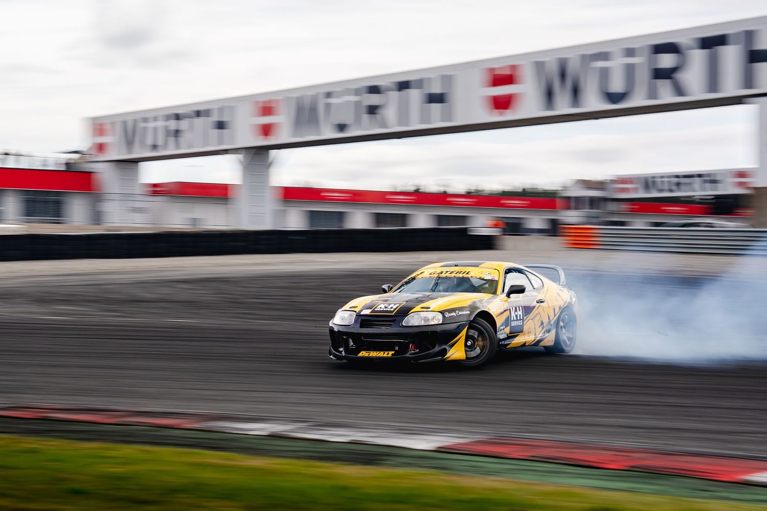 Race cars drift around a track corner in a high-speed motorsport competition at a professional racing circuit.