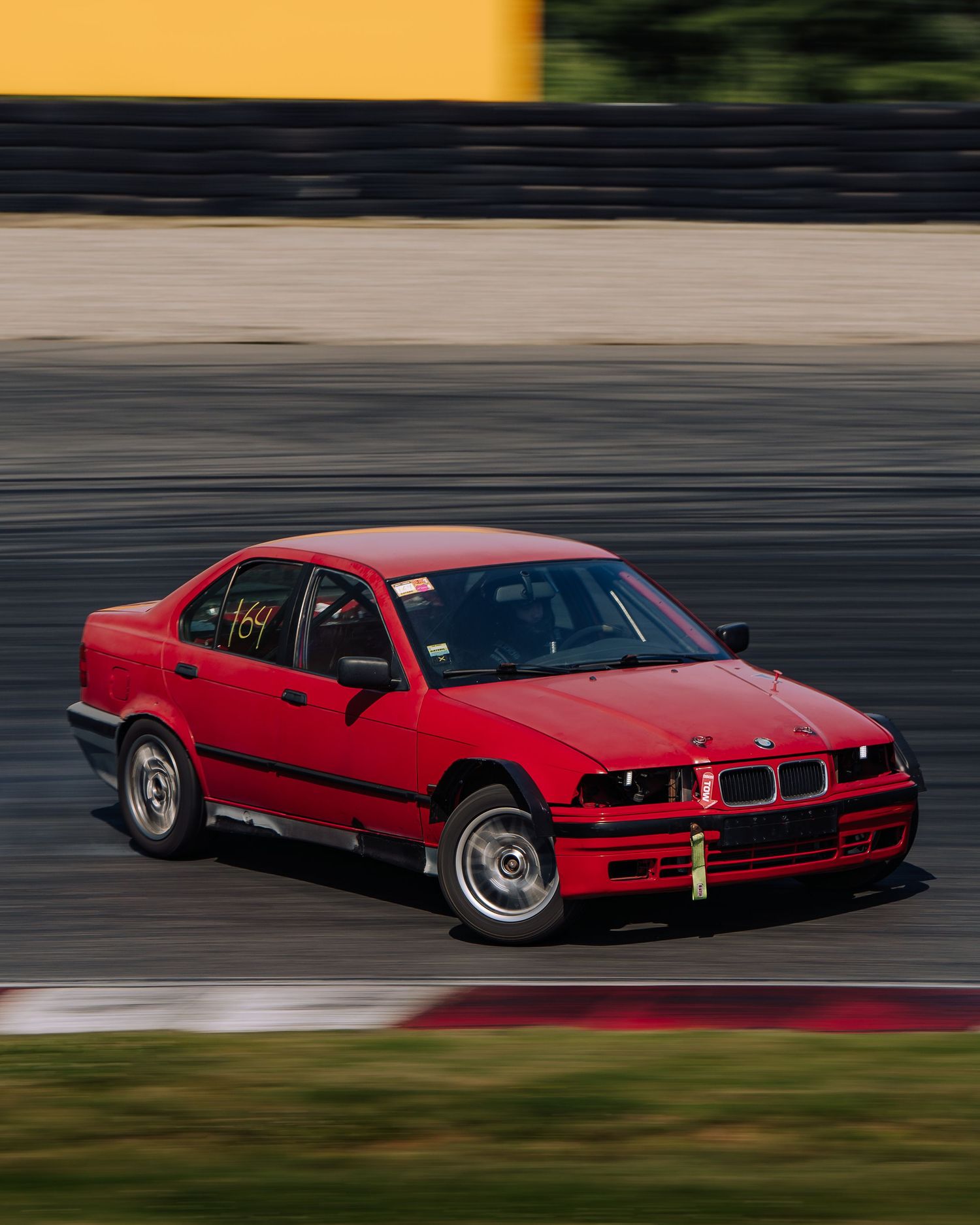 A red BMW M8 race car drifting on a racetrack with motion blur showing high-speed movement.