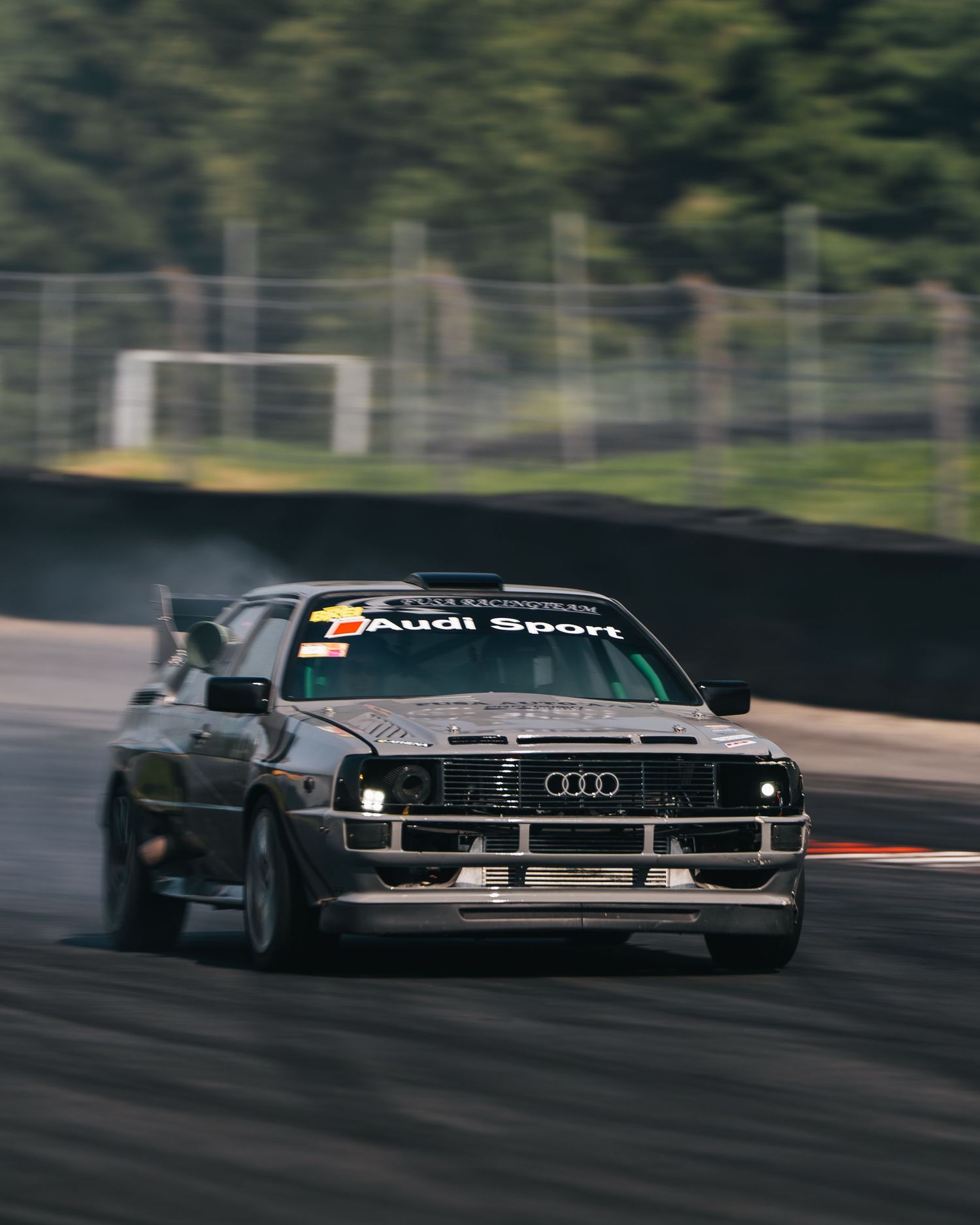 A vintage Audi Sport car drifting on a race track with smoke trailing from its tires during a motorsport event.