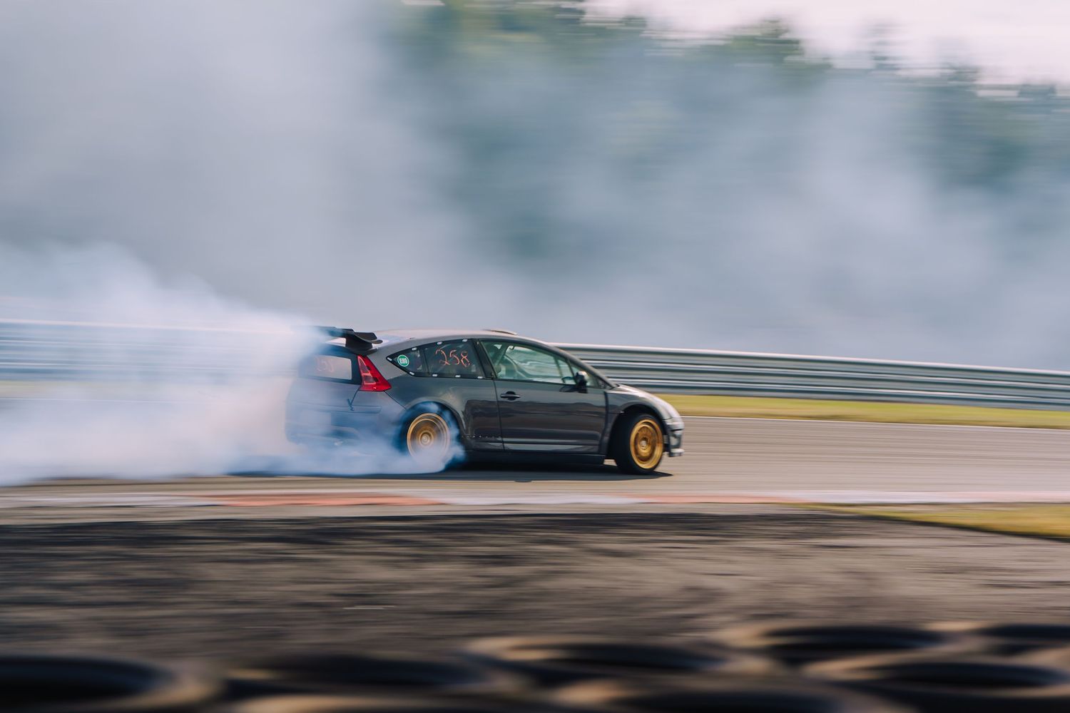 A sports car drifts on a racetrack creating clouds of white tire smoke during a performance run.