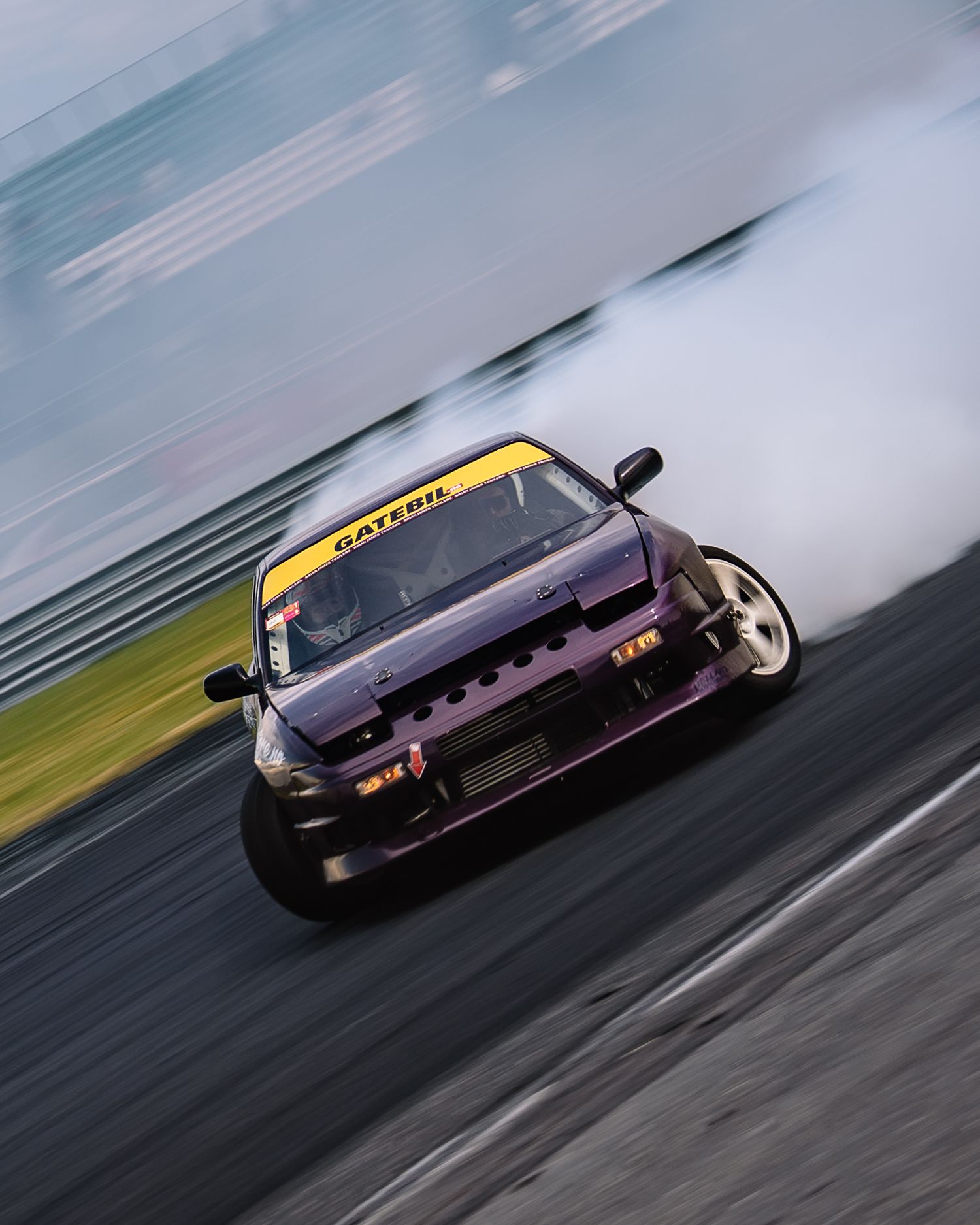 A purple sports car drifting sideways on a race track with smoke billowing from the tires during a drift competition.