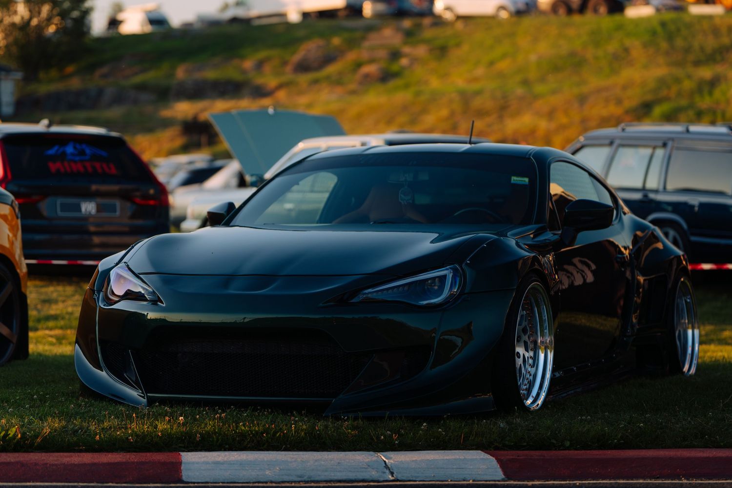 A sleek black sports car silhouetted against a sunset sky with dramatic lighting and reflective surfaces.