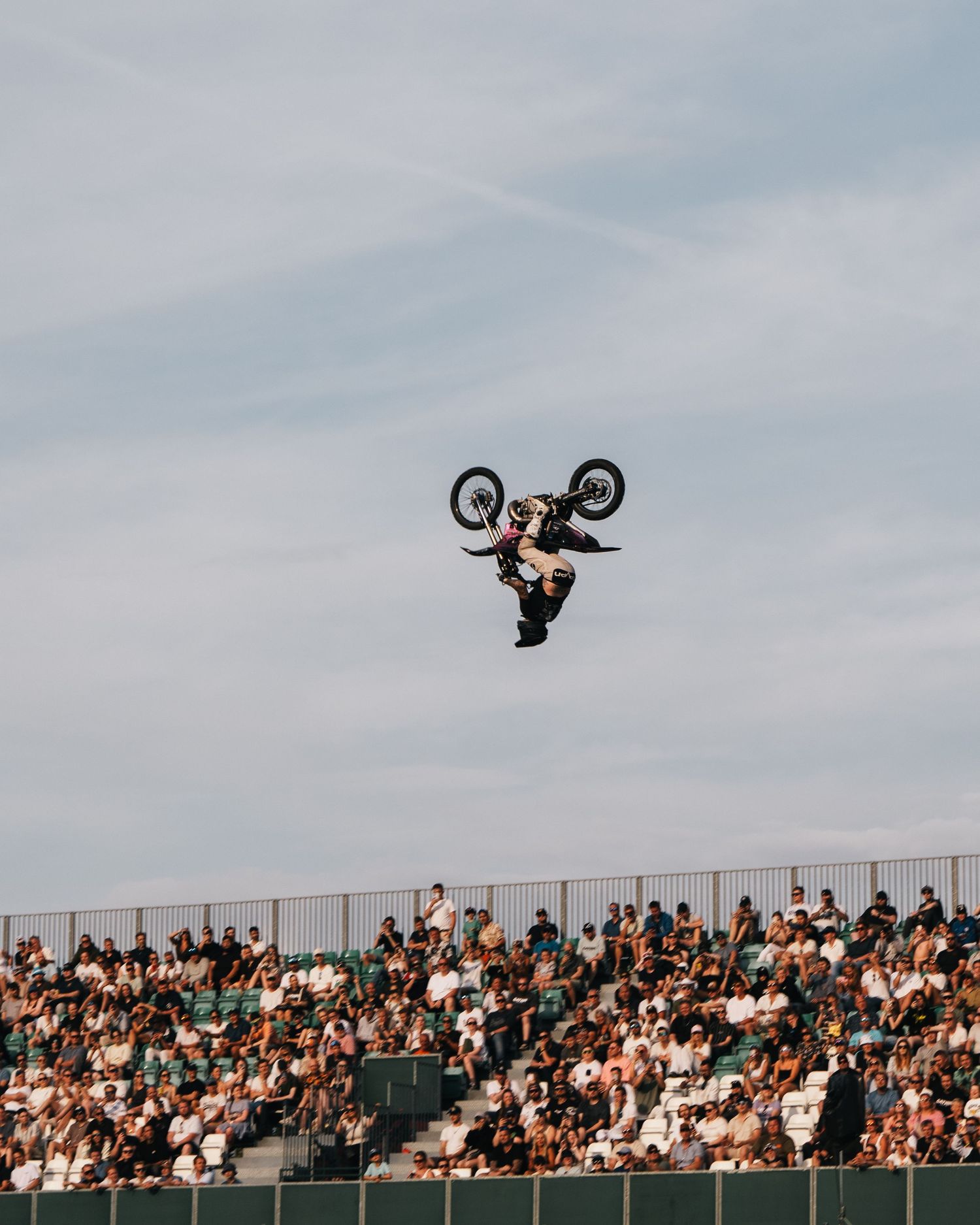 BMX rider performs a dramatic backflip high above the crowd during an extreme sports competition.