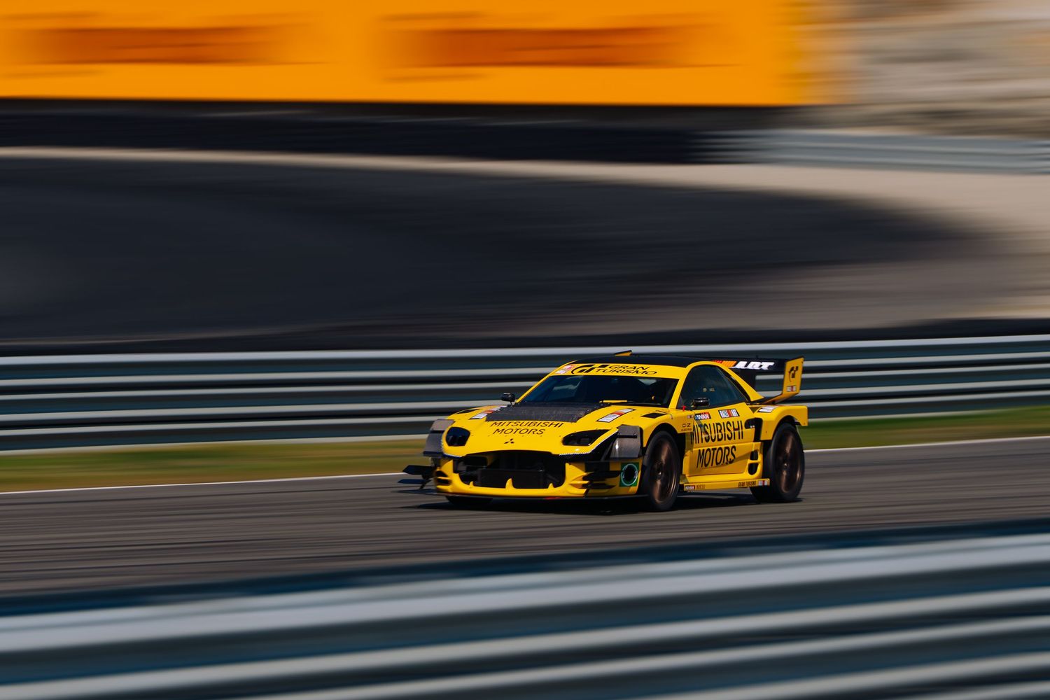 Yellow race car speeds along a racetrack with motion blur, showcasing dynamic motorsport action.