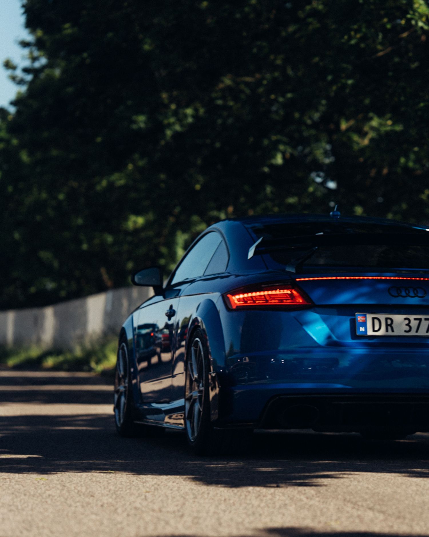 A sleek blue sports car shown from multiple angles on a sunny day with trees in the background.