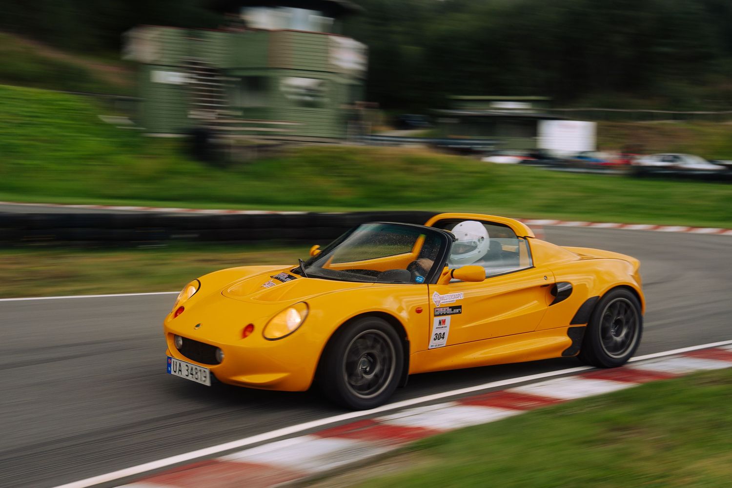 Yellow Lotus Elise sports car racing on a winding track with red and white curbing along the edge.