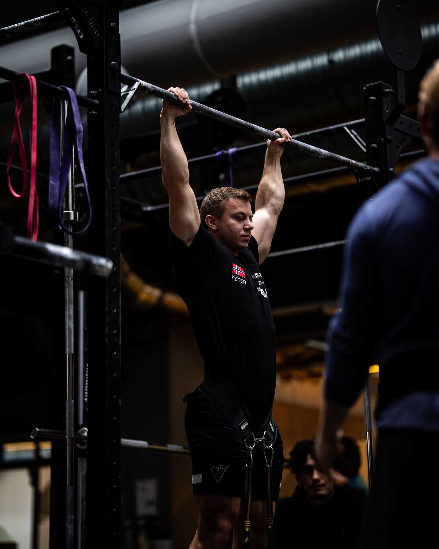 Athletes training on pull-up bars in a dimly lit fitness facility.
