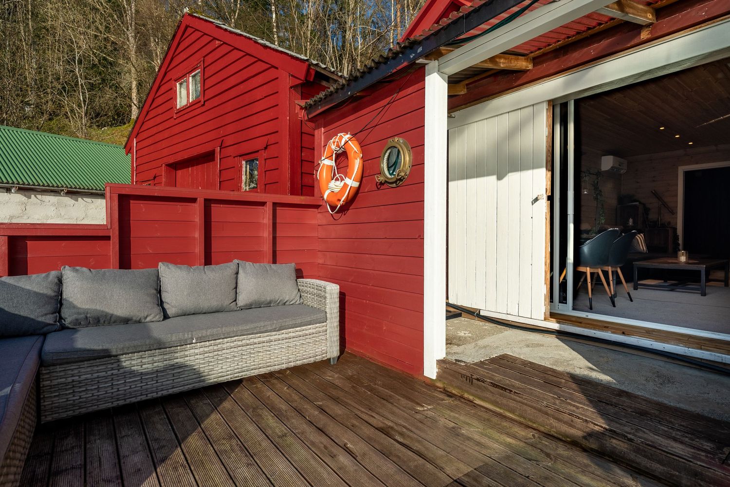A cozy red boathouse deck with grey outdoor seating and white trim overlooking the water.