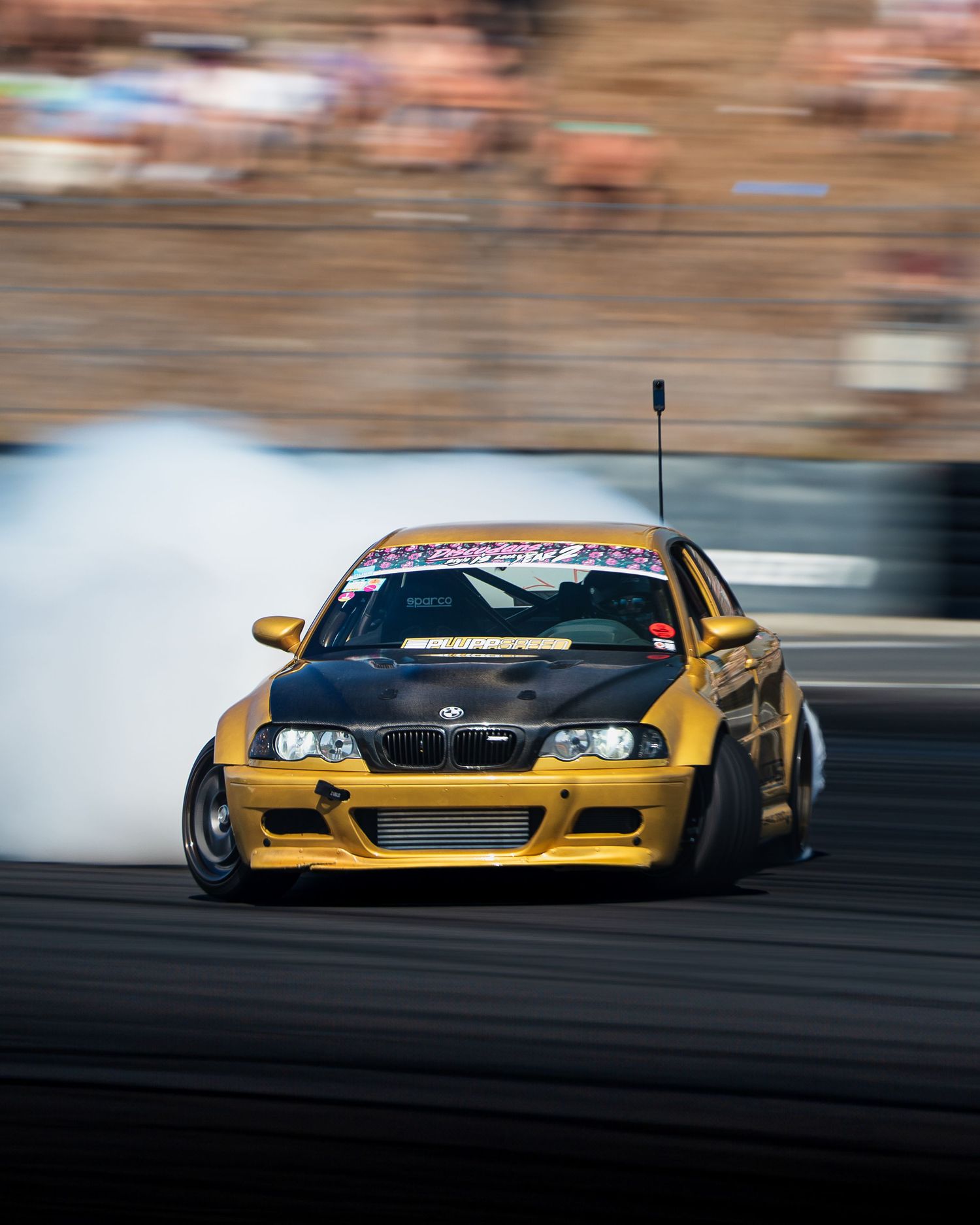 Yellow drift racing car slides sideways creating smoke on asphalt track during competitive motorsport event.