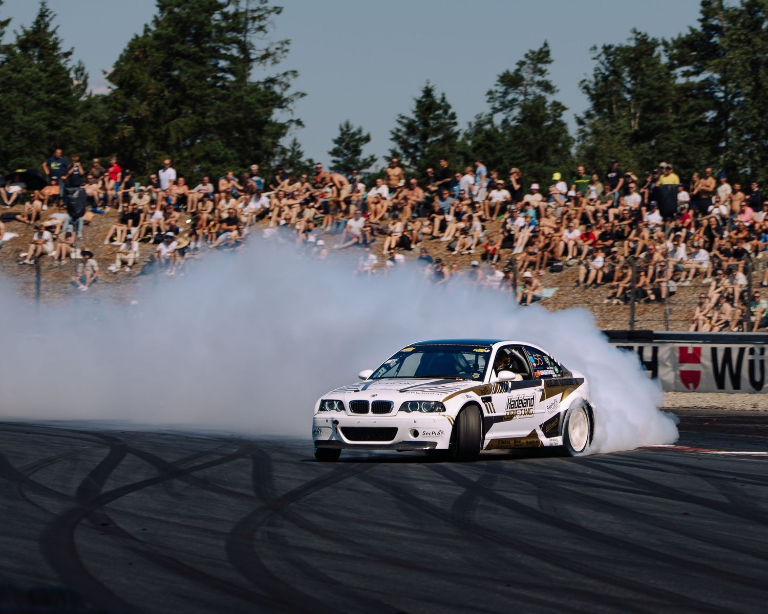 Drift cars perform a synchronized smoke-filled tandem run on a racetrack as spectators watch from packed grandstands.