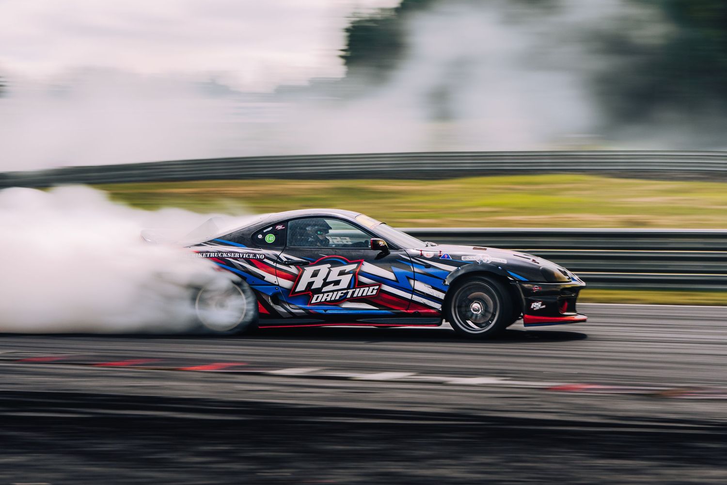 A race car speeds along a track creating motion blur as it drifts through a turn during a competition.
