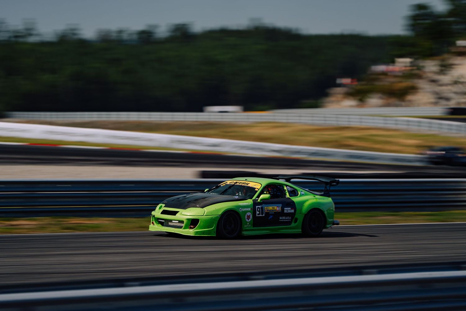 A bright green race car speeds around a racetrack with motion blur during a motorsport competition.