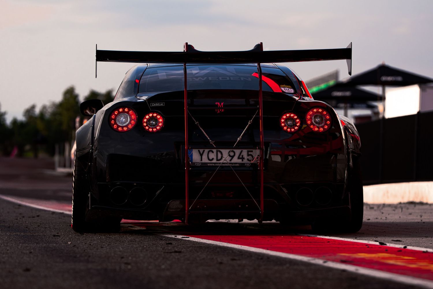 A row of red LED taillights glowing in the dark on multiple sports cars at a racing track.