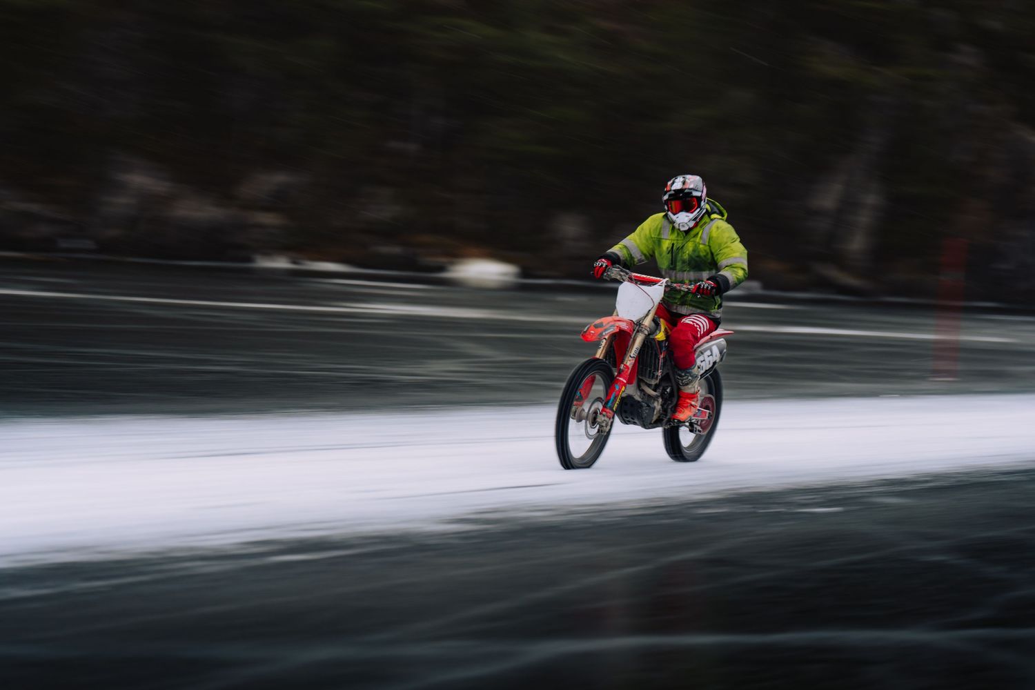 Red motorcycle speeds across snowy terrain leaving motion blur trails on a winter road.