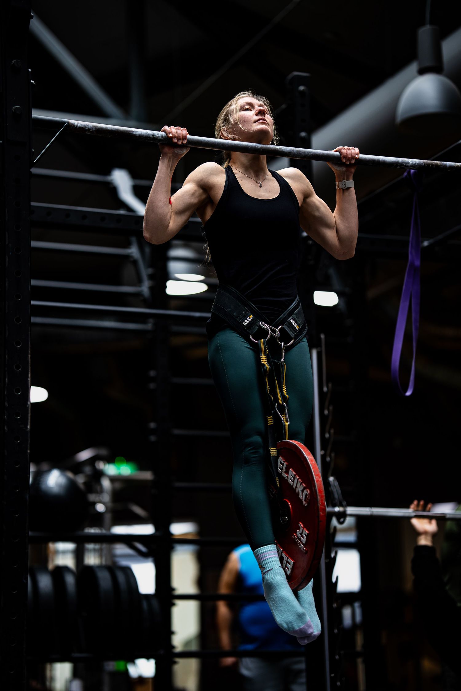 Person performing pull-ups on a gym bar with dramatic lighting effects.