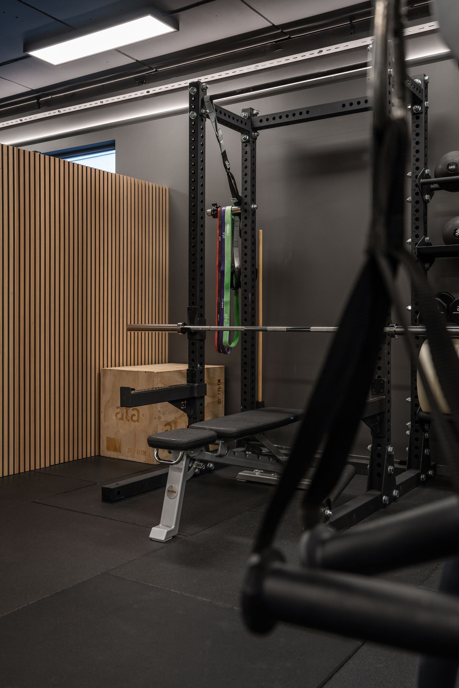 Power rack setup with bench press and wooden slat wall in a modern gym.