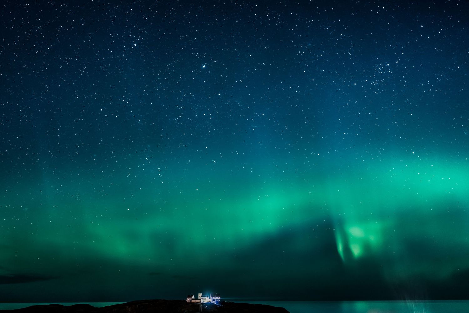 Spectacular aurora borealis display with swirling green lights over a distant lighthouse.