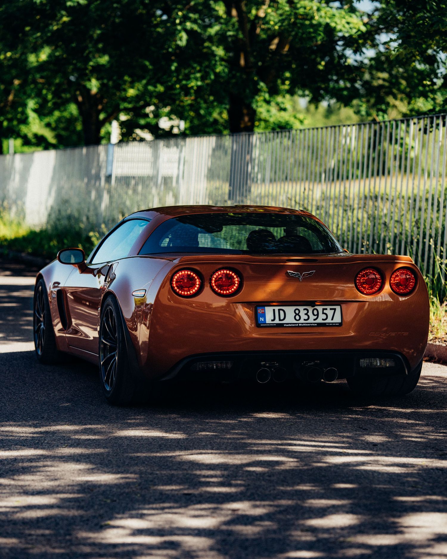 Modern red sports car with glowing taillights parked in a shady outdoor setting.