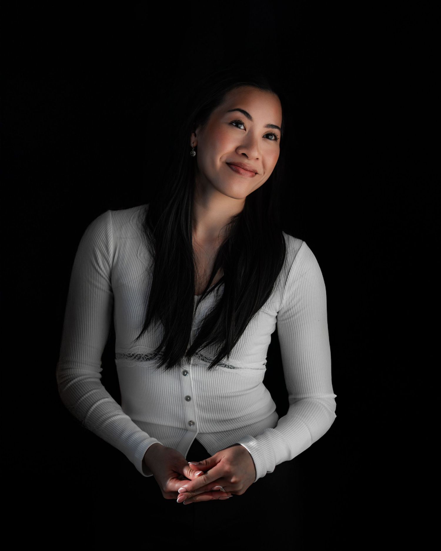 Fashion portrait on black background in dramatic lighting of someone wearing a white button-up cardigan.