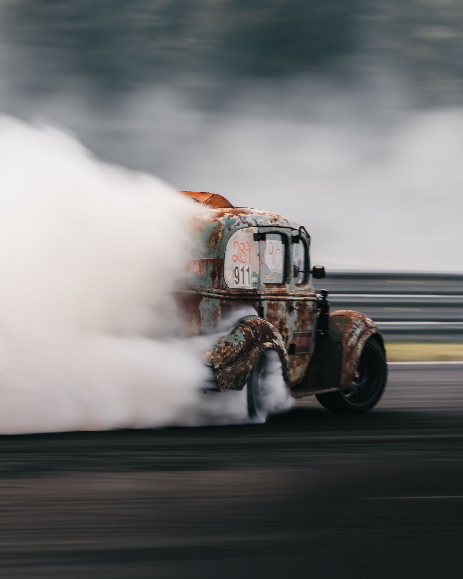 A race car performs a high-speed drift creating dramatic smoke trails on the track during a motorsport event.