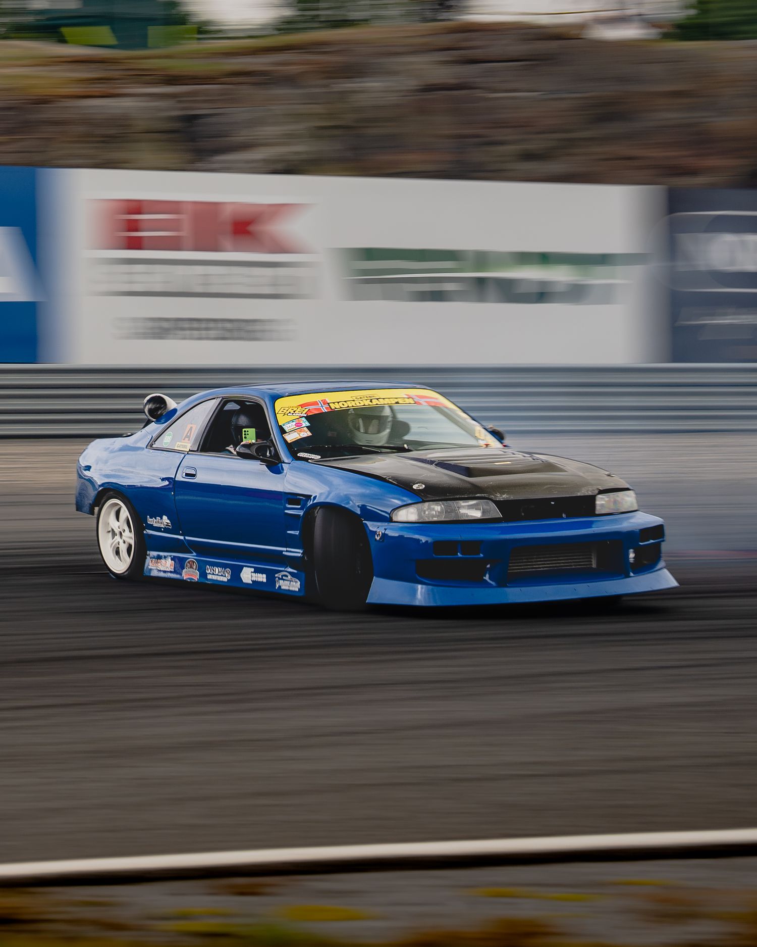 Blue drift car racing sideways on track with motion blur showing high speed performance driving action.