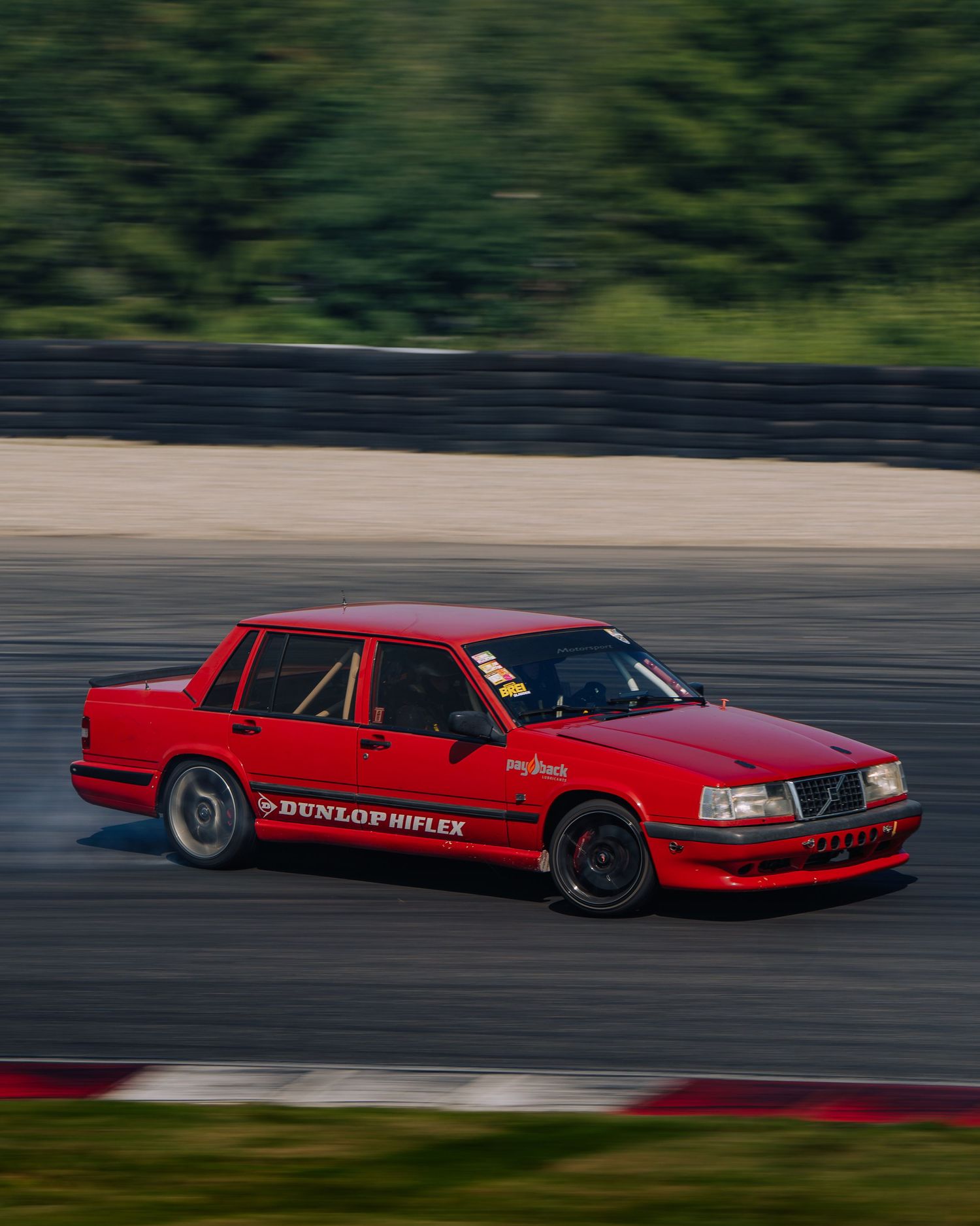 Red Volvo 850 sedan drifting on a racetrack with blurred forest background.