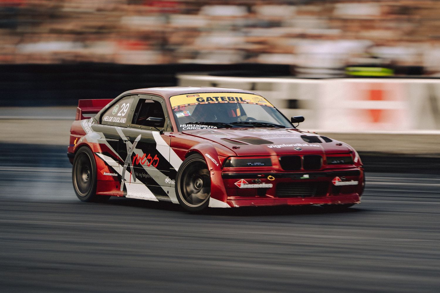 Red racing cars drift around a track during a competitive motorsport event.