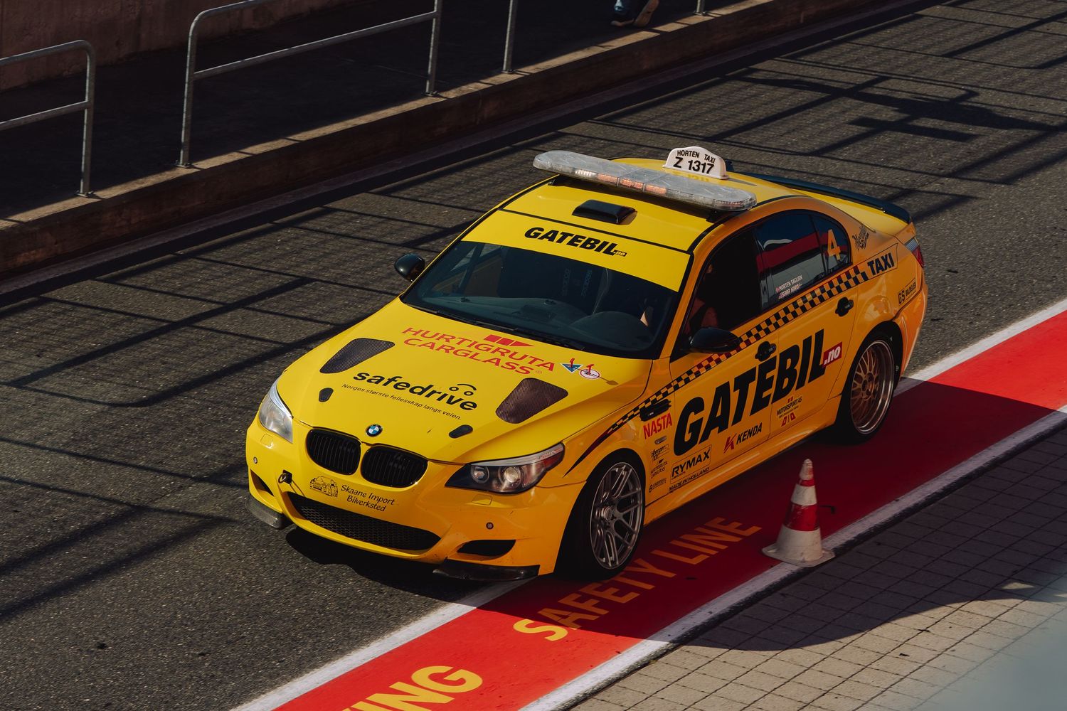 Yellow BMW M3 taxi racing cars lined up on a track with red and white curbing.