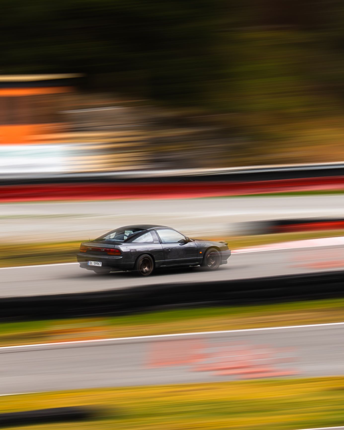 Motion-blurred black car racing on a track with vibrant autumn colors in the background.