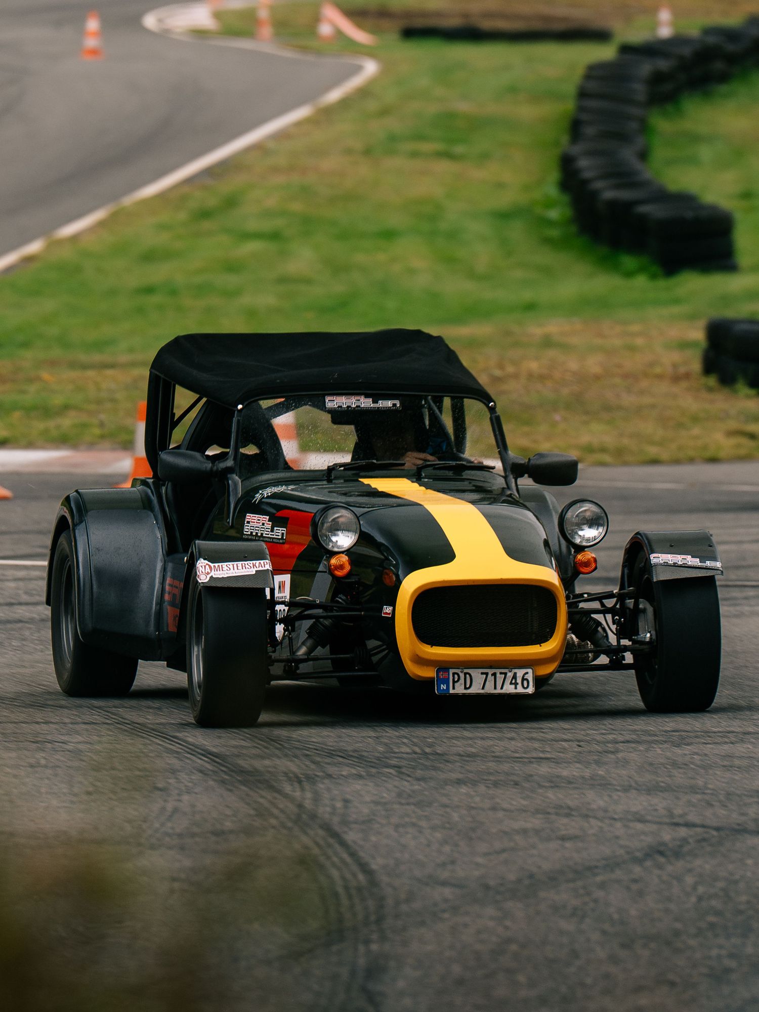 Four vintage racing cars navigate a curved racetrack with orange cones marking the course during a motorsport event.