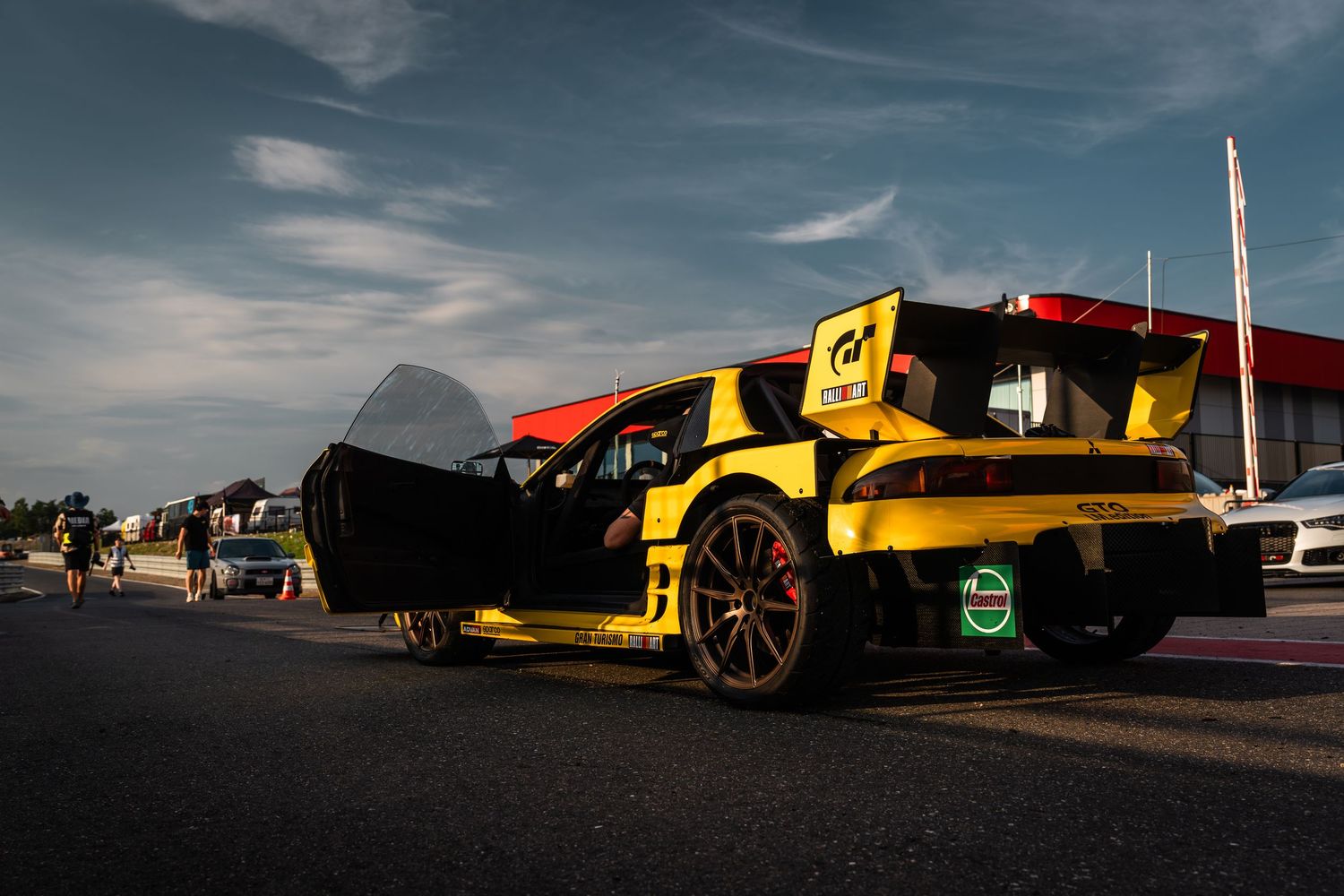 A yellow and black sports car photographed in a dramatic low angle silhouette against a moody sky at sunset.