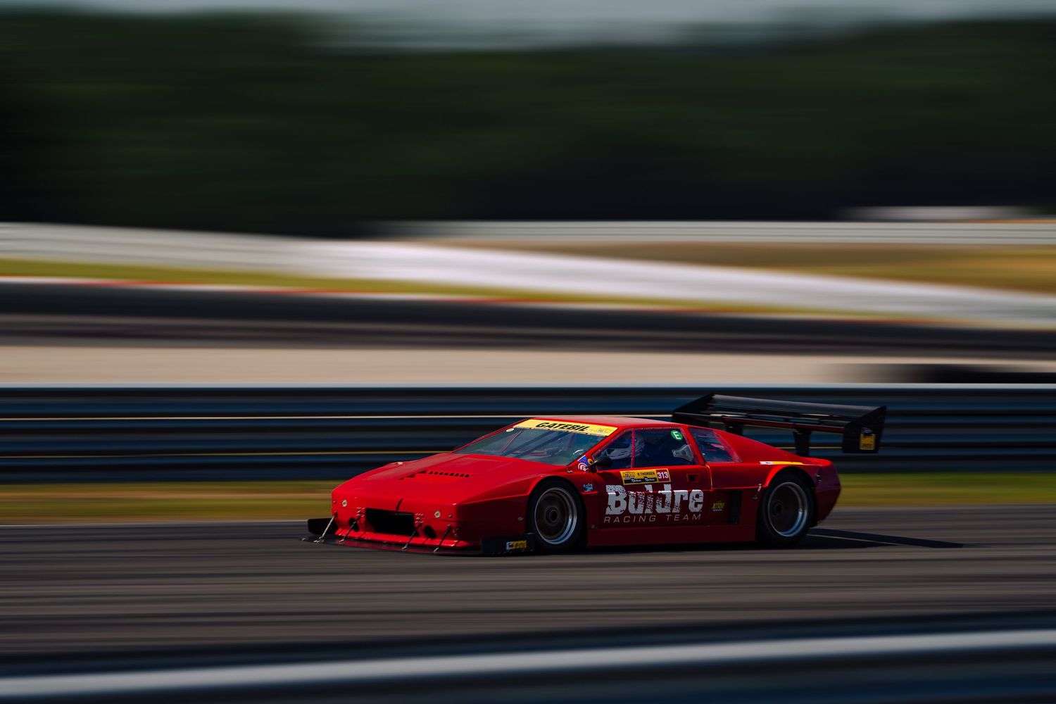 Red racing car speeds along racetrack with motion blur effect creating dynamic racing atmosphere.