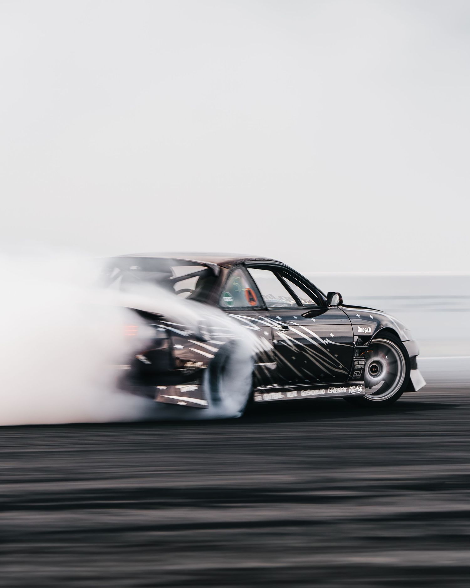 Black sports car drifting on track with smoke trailing behind creating dramatic motion blur effect.