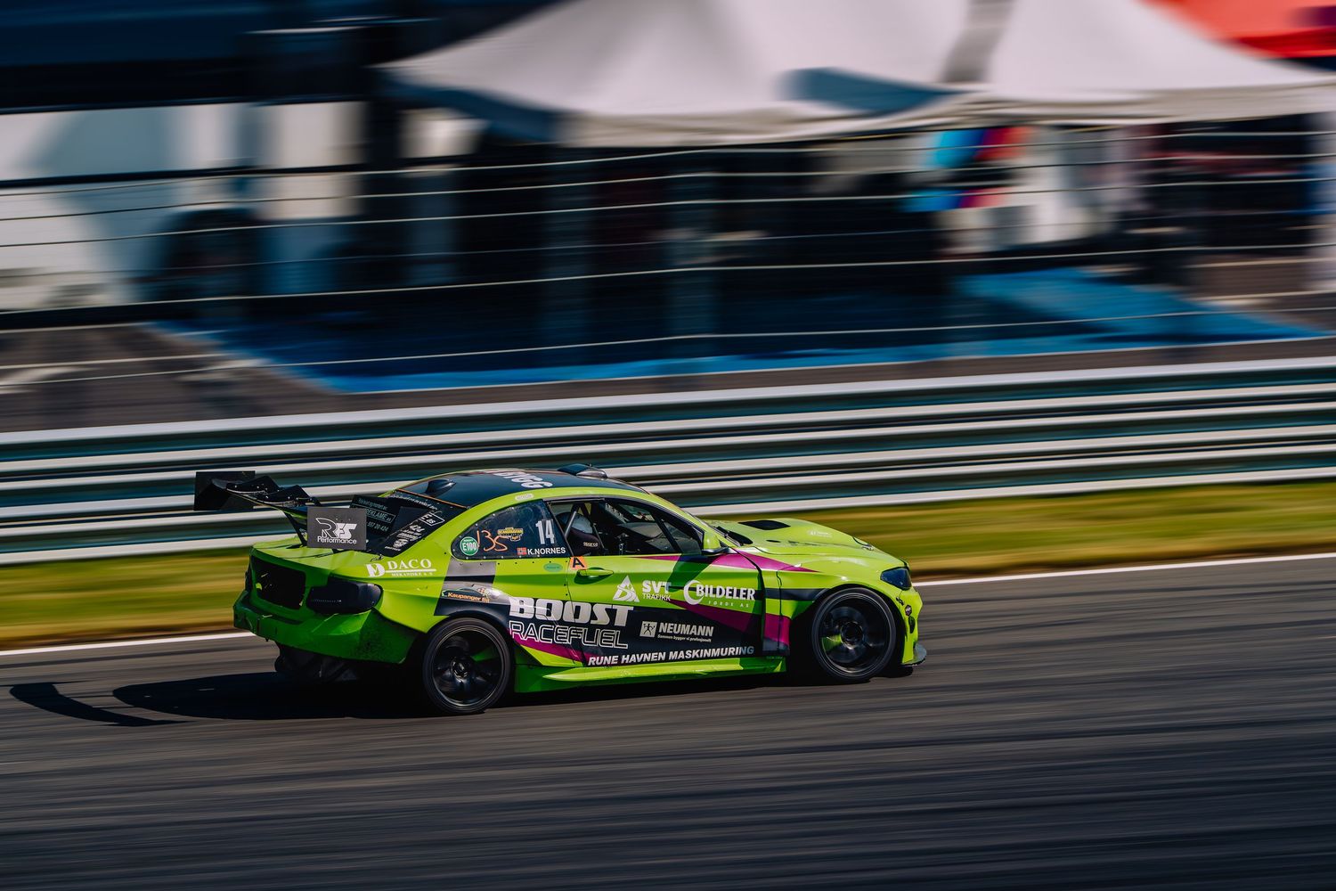 Green drift racing car sliding sideways on a racetrack during a professional motorsport competition event.