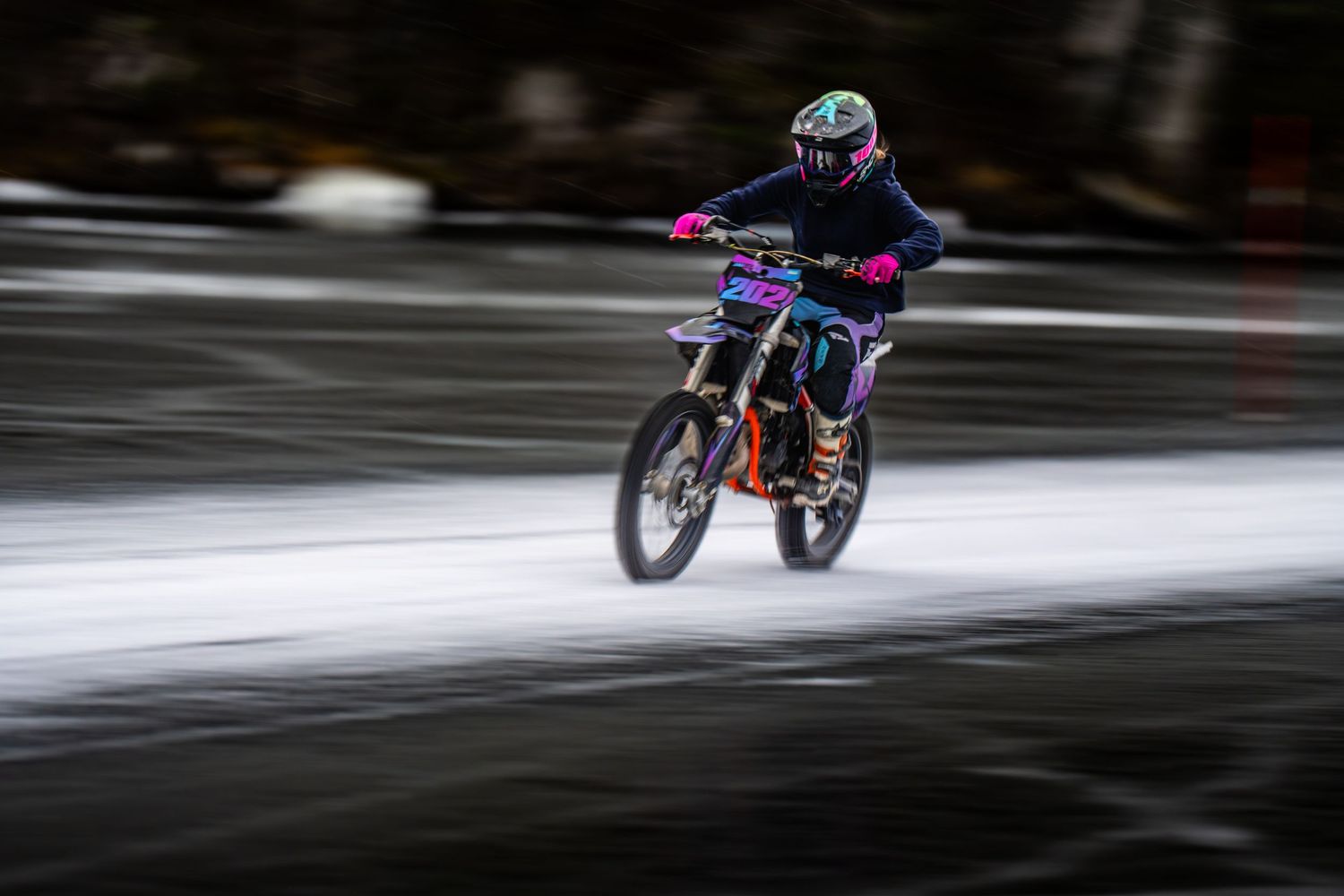 A motorcycle rider performs a dramatic jump sequence across snowy terrain during a winter motorsport event.